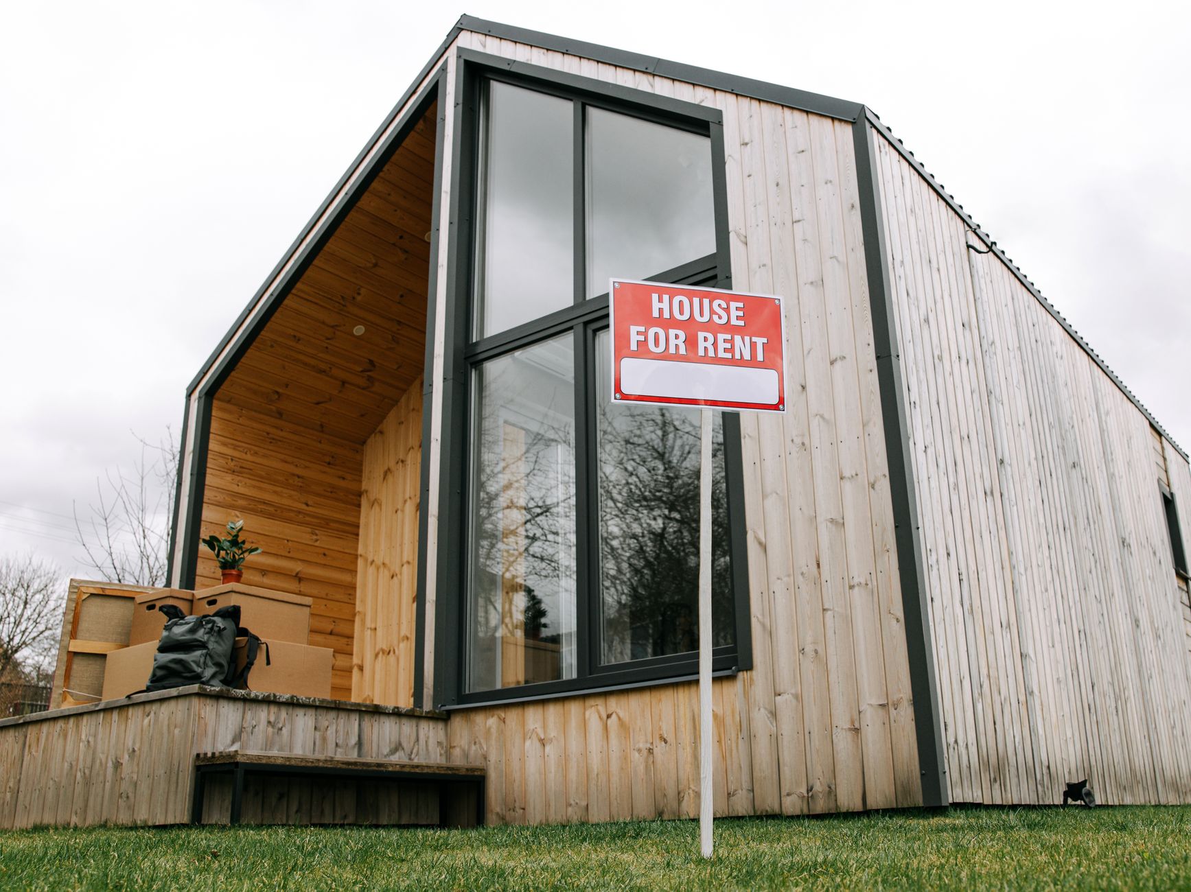 A timber clad house with a house for rent sign outside